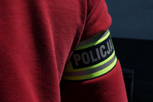 Na kolorowym zdjęciu widoczna opaska z napisem POLICJA, założona na ramię policjanta.