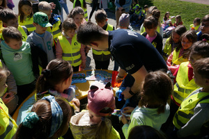 Na kolorowym zdjęciu widoczny policjant wśród dzieci, które mają założone kamizelki odblaskowe.