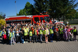 Kolorowe zdjęcie grupowe. Dzieci z przedstawicielami służb mundurowych. W tle wóz strażacki.