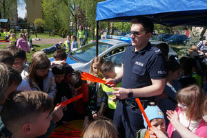 Na kolorowym zdjęciu widoczny policjant rozdający dzieciom odblaski.