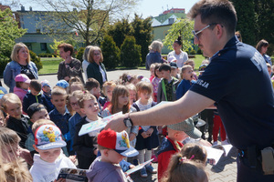 Na kolorowym zdjęciu widoczny policjant rozdający dzieciom kolorowanki.