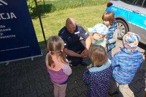 Na kolorowym zdjęciu widoczny policjant rozmawiający z dziećmi.