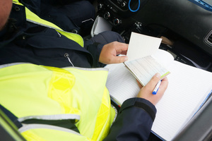 Policjant trzyma w ręku bloczek mandatowy,