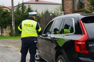 Policjant podczas kontroli drogowej stoi obok czarnego samochodu.