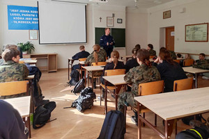 Na zdjęciu widoczny umundurowany policjant prowadzący zajęcia z uczniami w mundurach.