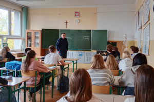 Na zdjęciu widoczny umundurowany policjant, prowadzący prelekcję dla młodzieży.