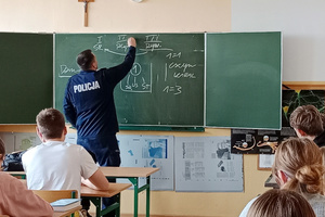 Na zdjęciu widoczny umundurowany policjant, prowadzący prelekcję dla młodzieży.