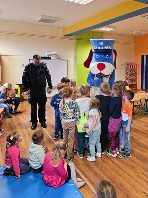 Na zdjęciu umundurowany policjant wraz ze Sznupkiem i przedszkolakami.