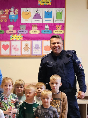 Na zdjęciu umundurowany policjant pozujący do zdjęcia wraz z przedszkolakami.