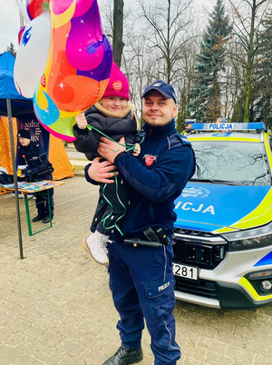 Na zdjęciu widoczny policjant trzymający na rękach dziecko.