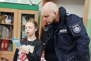 Na zdjęciu widoczny policjant, który z dziewczynką czyta ulotkę informacyjną.