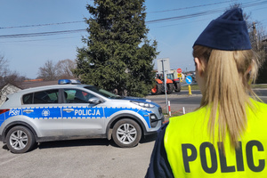 Na zdjęciu widoczna umundurowana policjantka, radiowóz oraz ustawiony na jezdni ciągnik rolniczy.