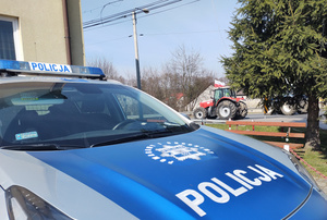 Na zdjęciu widoczny radiowóz, a za nim ustawiony na jezdni ciągnik rolniczy.