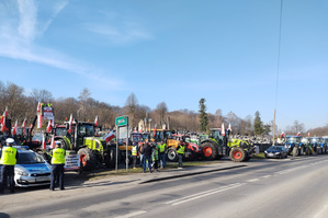 Na zdjęciu widoczny radiowóz, umundurowani policjanci oraz osoby biorące udział w zgromadzeniu. Widoczne też ciągniki rolnicze.