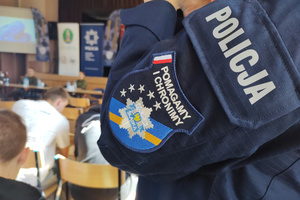 Na zdjęciu widoczna częściowo umundurowana policjantka, na której rękawie widoczny napis: POLICJA oraz naszywka z napisem: POMAGAMY I CHRONIMY i grafika policyjnej gwiazdy.