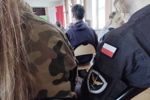 Na zdjęciu widoczne częściowo uczennice w mundurach. Na rękawie jednego z nich widoczne naszywki w postaci polskiej flagi oraz logo szkoły.