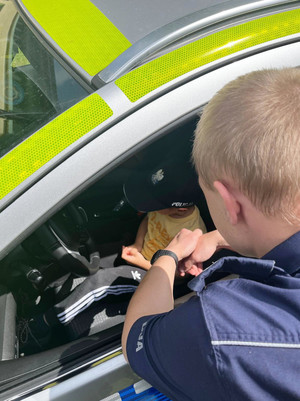 Na zdjęciu widoczne dziecko siedzące w radiowozie. Obok stoi policjant.