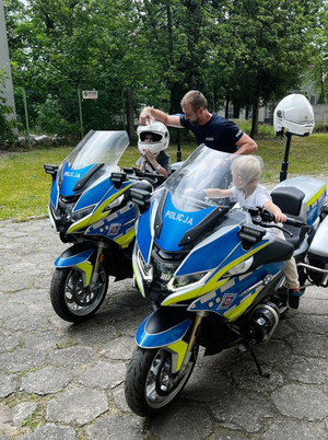 Na zdjęciu widoczne dzieci siedzące na policyjnych motocyklach. Obok stoi policjant.