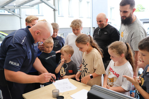 Na zdjęciu widoczny policjant, który ujawnia ślady daktyloskopijne. Wokół niego zgromadzone są dzieci.