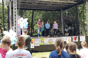 Na zdjęciu widoczna scena i znajdujące się na niej osoby. Przed sceną stoją dzieci.