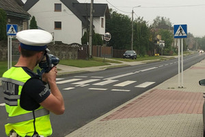 Na zdjęciu widoczny policjant, który mierzy prędkość nadjeżdżającego pojazdu.