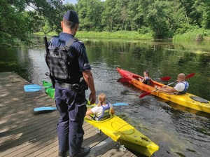 Dwaj kajakarze w kajakach, na pomoście policjant.