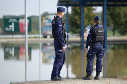 Na zdjęciu widoczna policjantka i policjant, którzy obserwują podtopiony teren.