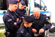 Na zdjęciu widoczni trzej policjanci i policjantka, którzy patrzą na smartfon.