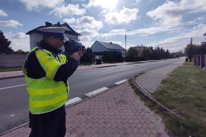 Na zdjęciu widoczny policjant, który mierzy prędkość nadjeżdżającego pojazdu.