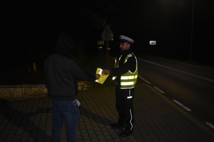 Na zdjęciu widoczny policjant, który przekazuje kamizelkę odblaskową pieszemu.