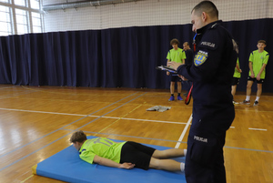 Na zdjęciu widoczni uczestnicy drugiego Trójboju policyjnego oraz policjant. Jeden z zawodników leży na macie.