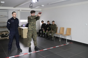 Na zdjęciu widoczni uczestnicy drugiego Trójboju policyjnego. Jeden z nich strzela na strzelnicy multimedialnej. Obok niego stoi policjant.