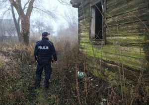 Policjant stoi przy opuszczonym budynku.