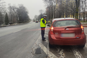 Na zdjęciu widoczny policjant podczas kontroli drogowej. Policjant stoi obok zatrzymanego pojazdu.