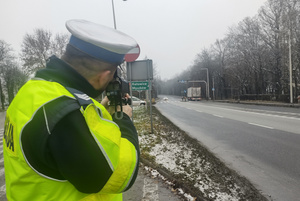 Na zdjęciu widoczny policjant, który mierzy prędkość jadącego pojazdu.