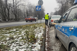 Na zdjęciu widoczny policjant podczas kontroli drogowej. Policjant stoi obok zatrzymanego pojazdu.