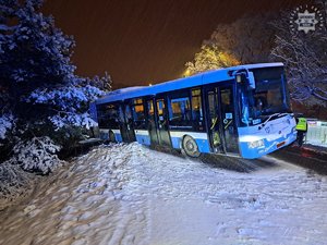 Na zdjęciu widoczny autobus stojący na zaśnieżonym poboczu, a także policjant, który idzie koło autobusu.