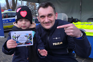 Na zdjęciu widoczny policjant i mały chłopiec, który w rękach trzyma ulotkę z napisem &quot;Zostań śląskim policjantem&quot;.