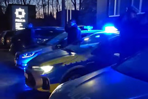 Na zdjęciu widoczne radiowozy z włączonymi niebieskimi światłami oraz policjanci oddający honor.