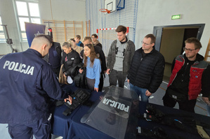 Na zdjęciu widoczny policjant, który prezentuje policyjny sprzęt uczestnikom spotkania.