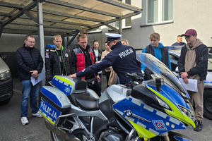 Na zdjęciu widoczny policjant z drogówki, który wskazuje na stojący obok motocykl. Wokół uczestnicy spotkania.
