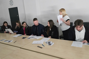 Na zdjęciu widoczni uczestnicy spotkania, którzy siedzą przy stole z ulotkami. Przedstawicielka Zespołu Kadr i Szkolenia rozdaje druki.
