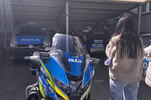 Na zdjęciu na pierwszym planie widoczny policyjny motocykl. Dalej widoczny policjant przy radiowozach. Wokół uczestnicy spotkania.