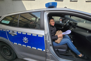 Na zdjęciu widoczna kobieta, która siedzi na miejscu pasażera w radiowozie.