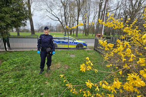 Na zdjęciu widoczna policjantka, która stoi przy zasadzonym drzewku. W tle widoczny radiowóz.