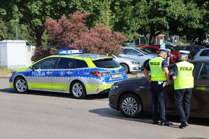 Na zdjęciu widoczny radiowóz oraz policjant i policjantka, podczas kontroli drogowej.