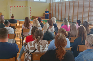 Na zdjęciu widoczny policjant oraz biorący udział w spotkaniu opiekunowie.