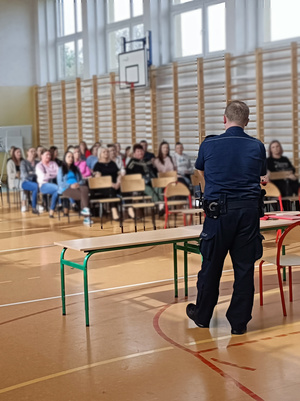 Na zdjęciu widoczny policjant oraz biorący udział w spotkaniu opiekunowie.