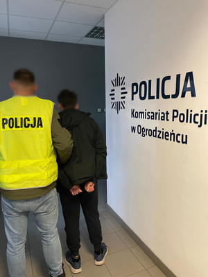 Na zdjęciu widoczny nieumundurowany policjant w kamizelce odblaskowej z napisem Policja oraz zatrzymany mężczyzna.