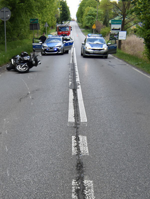 Na zdjęciu widoczny leżący na jezdni motocykl, za nim dwa radiowozy, za którymi jest również wóz strażacki.